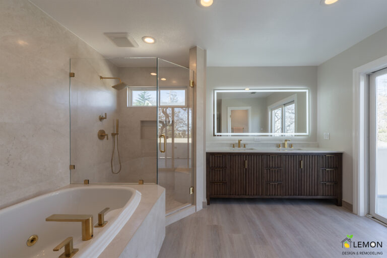 Modern luxury bathroom featuring a frameless glass walk-in shower, freestanding white soaking tub, dark wood double vanity with LED backlit mirror, brushed gold fixtures, porcelain tile walls, recessed lighting, and large windows bringing natural light into the space.